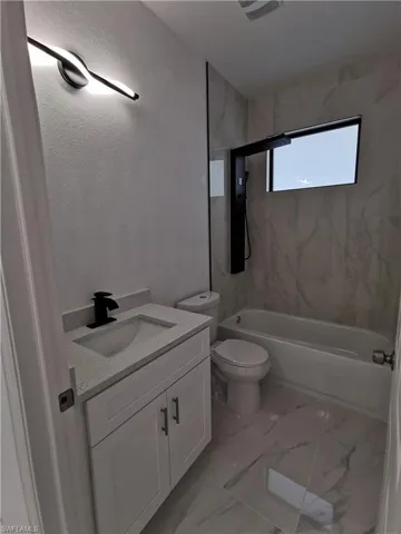 Bathroom featuring vanity, bathtub / shower combination, light marble finish flooring, and a textured wall