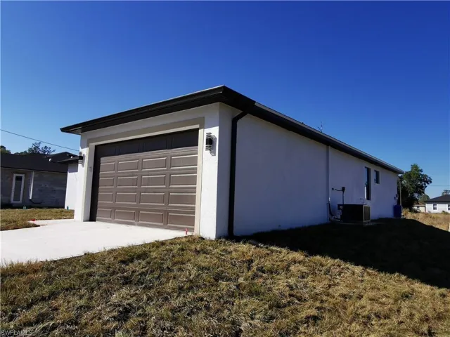 View of side of home with driveway, stucco siding, and a lawn
