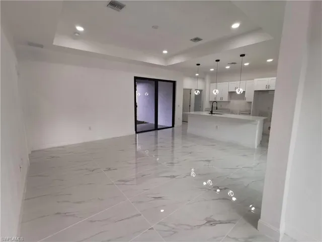 Unfurnished living room featuring a tray ceiling, recessed lighting, and light marble finish floors