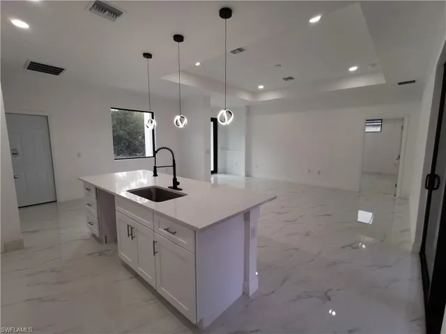 Kitchen with recessed lighting, white cabinetry, light stone counters, open floor plan, and a raised ceiling
