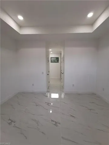 Empty room featuring a raised ceiling, recessed lighting, and light marble finish floors