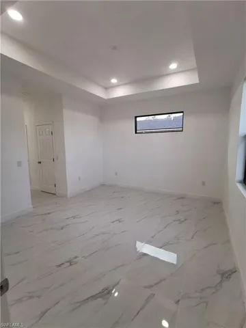 Empty room with recessed lighting, light marble finish flooring, and a tray ceiling