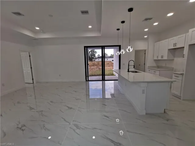 Kitchen with white cabinetry, pendant lighting, recessed lighting, a kitchen island with sink, and light stone counters