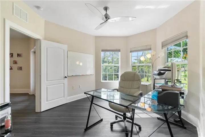 Home office with dark wood-style floors, baseboards, visible vents, and a ceiling fan
