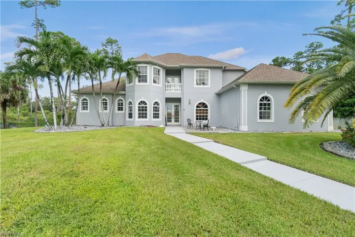 Rear view of house with french doors, a lawn, a balcony, and stucco siding