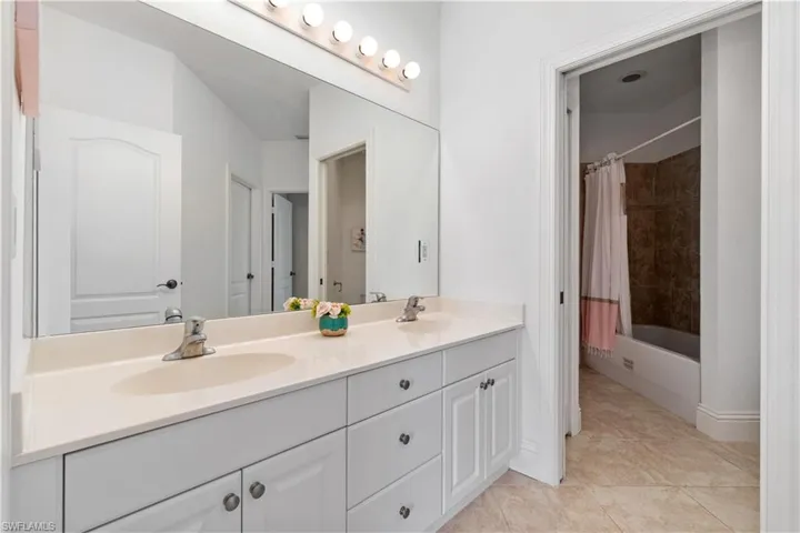Bathroom with shower / bath combo, tile patterned flooring, a sink, and double vanity