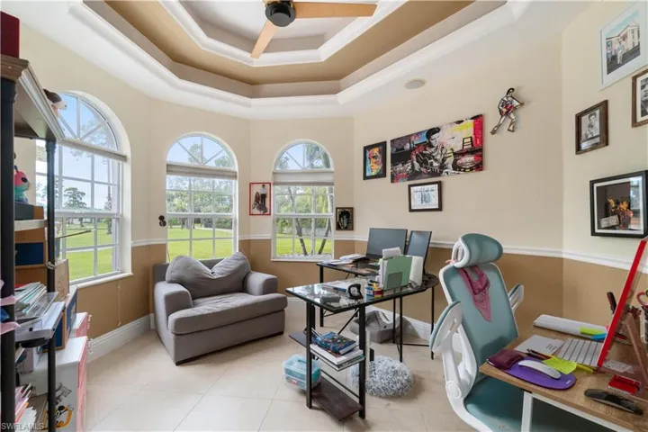 Office area with a raised ceiling, ceiling fan, and light tile patterned floors