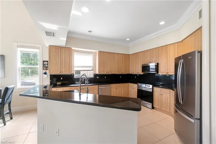 Kitchen with dark countertops, visible vents, stainless steel appliances, and light brown cabinetry