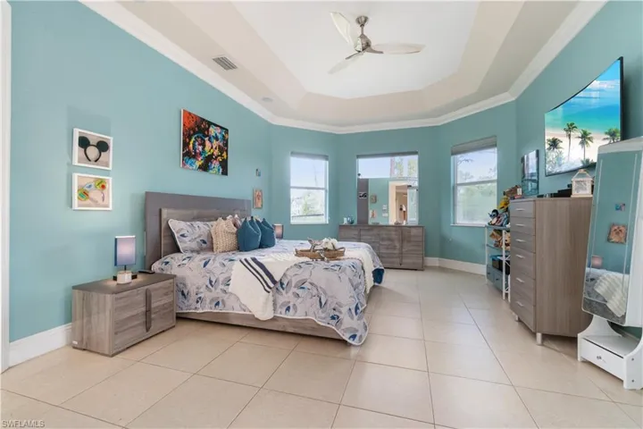 Tiled bedroom with crown molding, a raised ceiling, visible vents, a ceiling fan, and baseboards