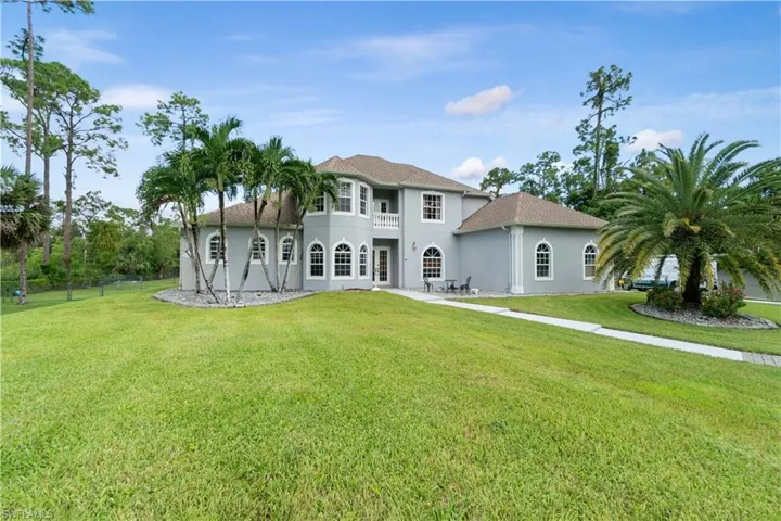 Rear view of property featuring a lawn, a balcony, and stucco siding
