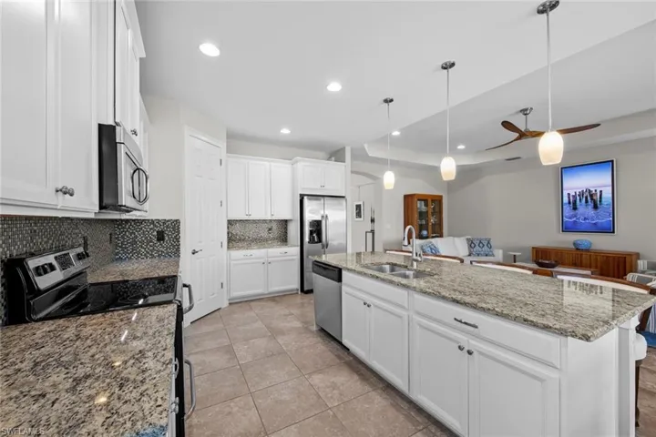 Open neutral kitchen with tile floor, staggered cabinets, granite counter tops, tile backsplash, cabinet crown molding, island pendants, under cabinet lighting, stainless steel appliances, and WALK-IN PANTRY.