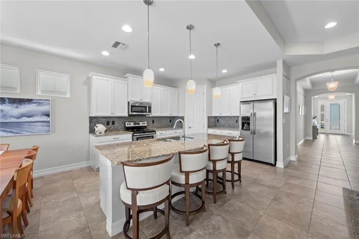 Open neutral kitchen with tile floor, staggered cabinets, granite counter tops, tile backsplash, cabinet crown molding, island pendants, under cabinet lighting, stainless steel appliances, and WALK-IN PANTRY.
