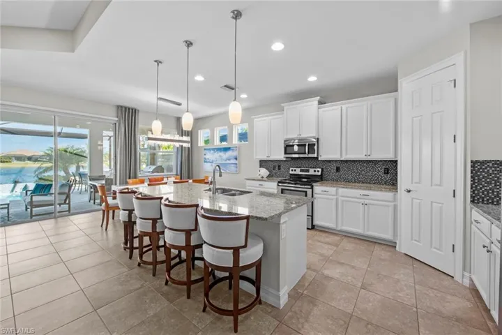 Open neutral kitchen with tile floor, staggered cabinets, granite counter tops, tile backsplash, cabinet crown molding, island pendants, under cabinet lighting, stainless steel appliances, and WALK-IN PANTRY.