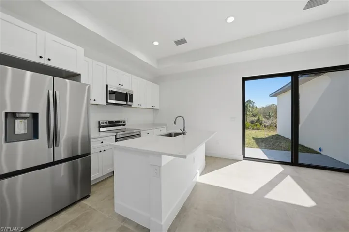Kitchen featuring stainless steel appliances, a kitchen island with sink, white cabinetry, recessed lighting, and light stone counters