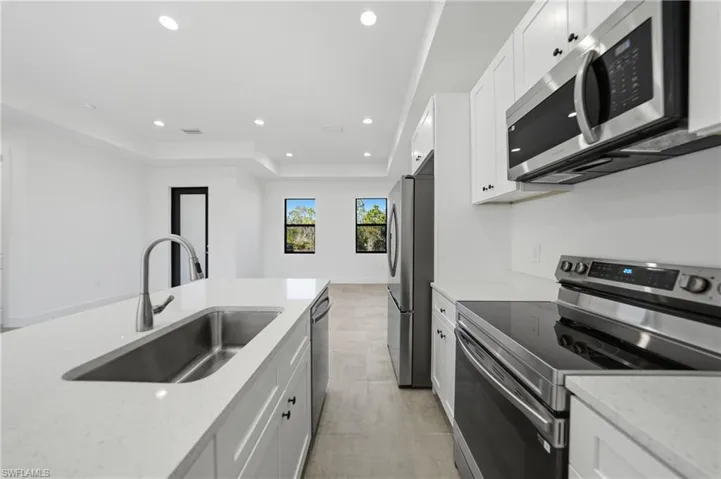 Kitchen featuring stainless steel appliances, a tray ceiling, white cabinetry, light stone countertops, and recessed lighting