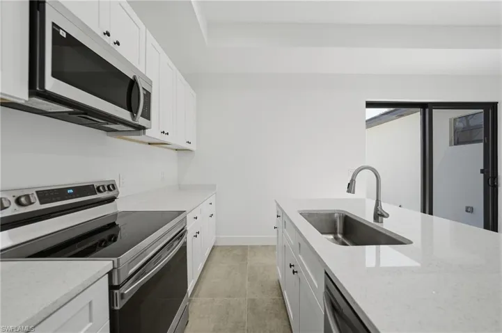 Kitchen with stainless steel appliances, white cabinetry, and light stone counters