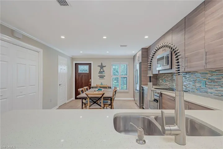 Kitchen with light stone countertops, stainless steel appliances, light wood-style flooring, tasteful backsplash, and ornamental molding. To the left in the picture ( closest to front door) is the guest bathroom and full size washer and dryer closet.