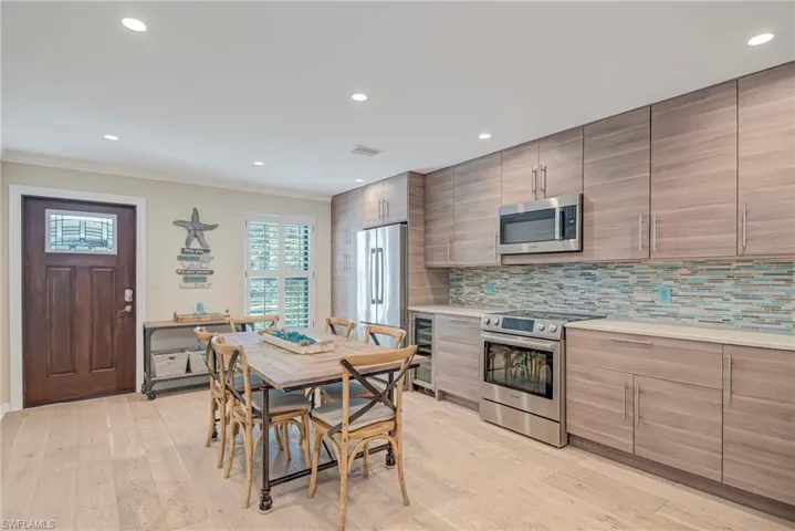 Gorgeous front door entry with stained glass panel, kitchen impact window with plantation shutters, dining space featuring recessed lighting, wine cooler, updated cabinets and counter, and light wood-style flooring