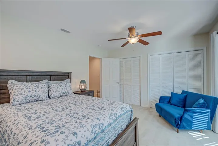 Bedroom with two closets, light colored carpet, and a ceiling fan