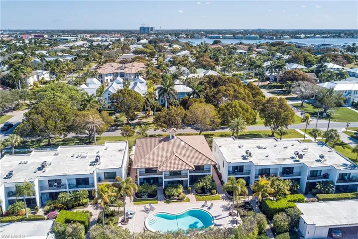 Drone / aerial view of a pool with the complex behind. Carport and extra storage for the unit is on the right hand side in the middle.