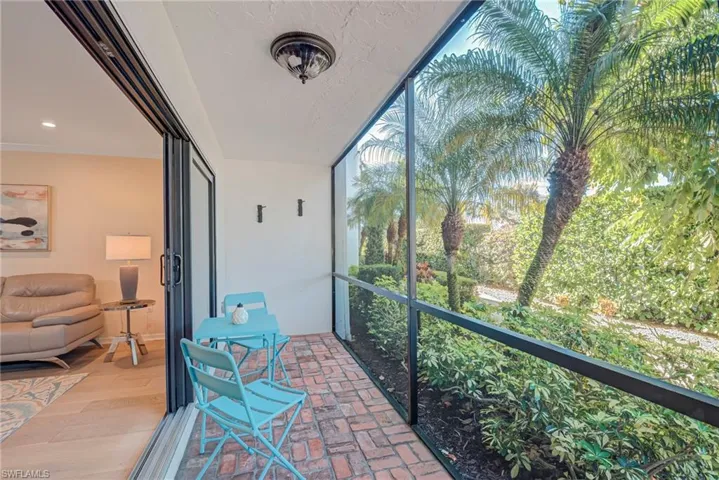 Screened-in lanai patio space that has a fan and bike hooks- this leads to the pathway to the pool, carport, and guest parking in the back of the building Lush palms and landscaping as your view!