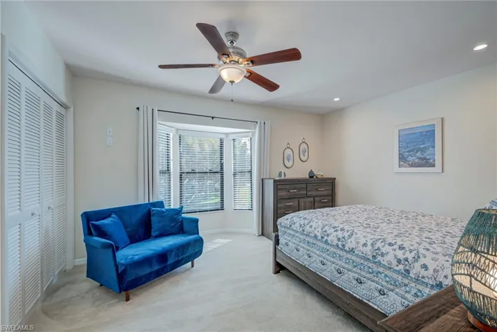 Awesome window with tons of natural light coming in and views of the trees swaying outside. Carpeted bedroom featuring a ceiling fan, 2 closets, window treatments, and recessed lighting. The bed is a queen and the couch is a sleeper sofa. There are two end tables next to the bed on both sides.
