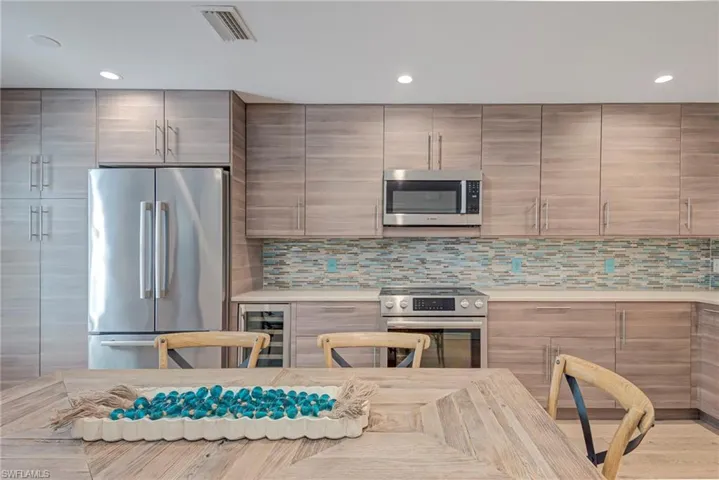 Kitchen with stainless steel appliances, wine cooler, backsplash, light stone counters, and recessed lighting