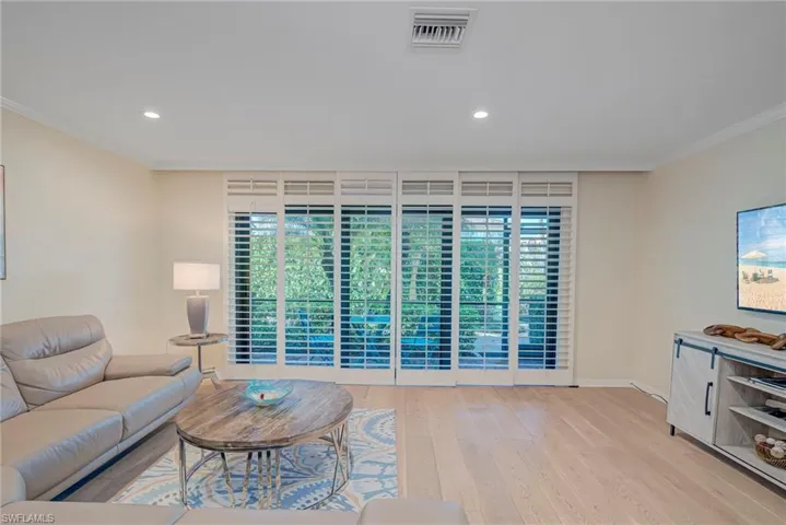 Living area with ornamental molding, light wood-style flooring, plenty of natural light, and recessed lighting. The plantation shutters are accordian and can moved to the wall - and provide extra privacy while also allowing the light to come in.