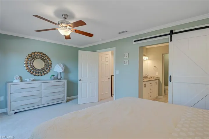 Bedroom featuring crown molding, a barn door, ceiling fan, light colored carpet, and ensuite bathroom featuring a barn door entry - double vanity, walk-in closet, and walk-in shower, toilet