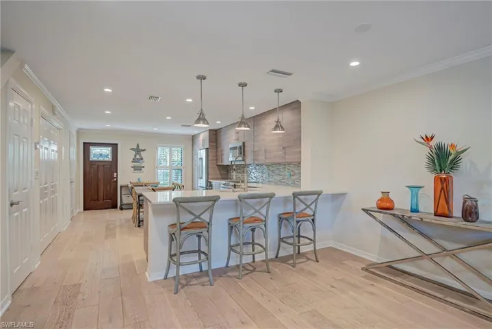Kitchen featuring a breakfast bar, ornamental molding, light stone countertops, hanging light fixtures, and plenty of space!