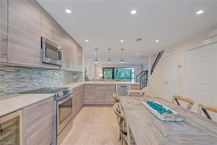 Kitchen featuring stainless steel appliances, modern cabinets, wine cooler, pendant lighting, and light stone countertops. There is a large walk-in pantry/storage closet and full washer and dryer ( on right). Guest bathroom is to the right as well.