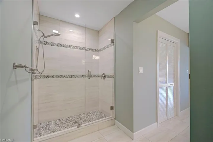 Bathroom featuring a shower stall, light tile patterned flooring, and recessed lighting- walk-in closet is also in the bathroom hallway across from the double sinks