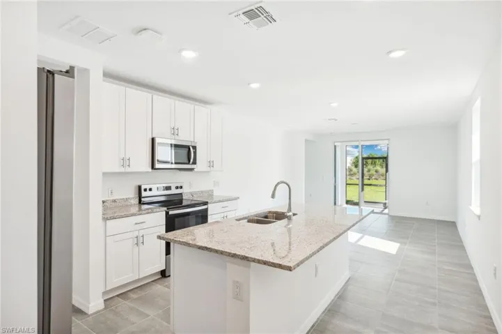 Kitchen with a kitchen island with sink, sink, light stone countertops, white cabinets, and appliances with stainless steel finishes