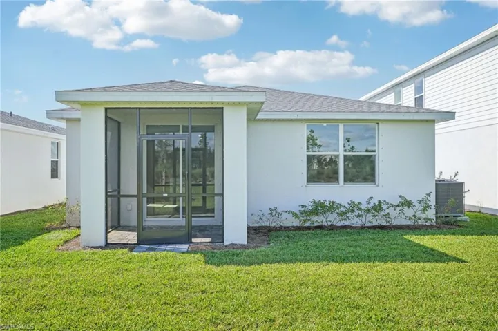 Rear view of house featuring a sunroom, a lawn, and central AC unit