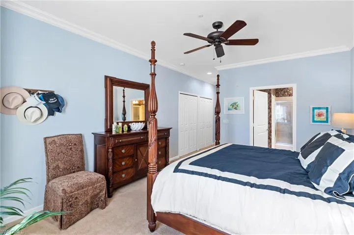 Bedroom with crown molding, ensuite bath, ceiling fan, light colored carpet, and a closet