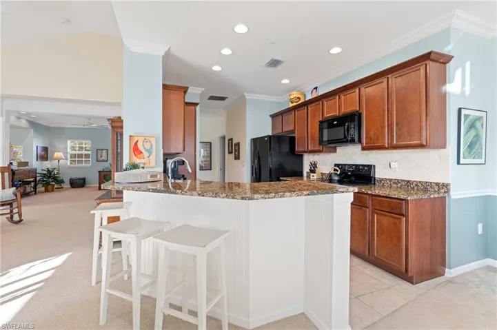 Kitchen featuring ceiling fan, dark stone countertops, light carpet, a breakfast bar, and black appliances