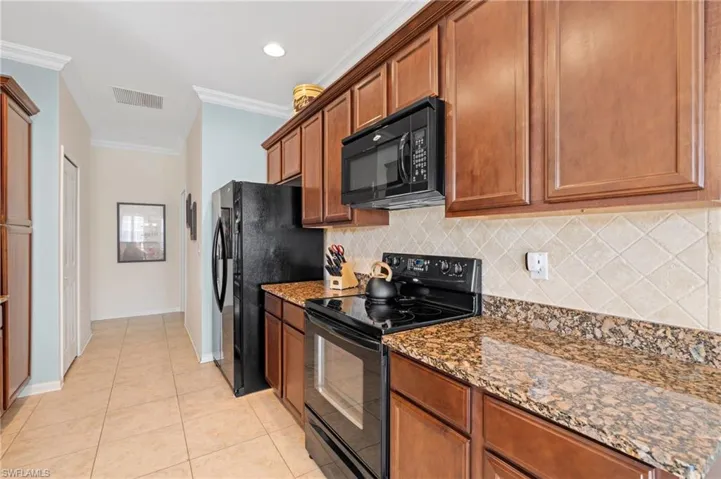 Kitchen with decorative backsplash, ornamental molding, black appliances, light tile patterned floors, and dark stone countertops