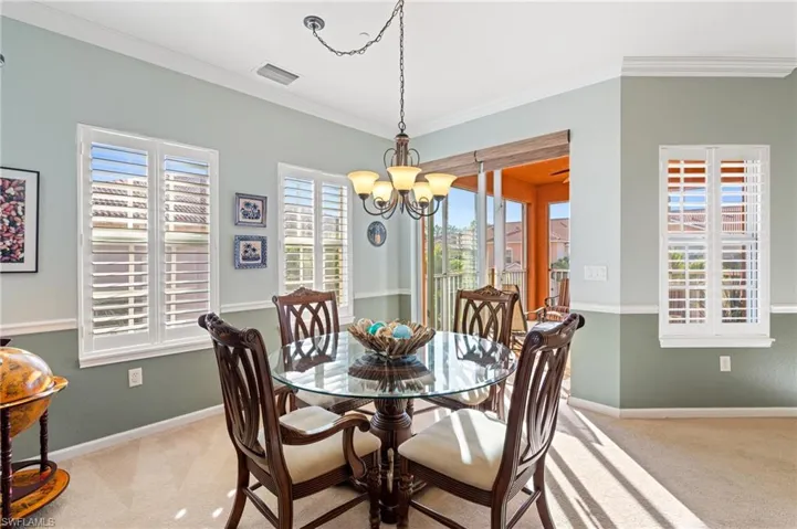 Carpeted dining area with ornamental molding and an inviting chandelier