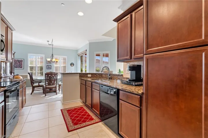 Kitchen with sink, hanging light fixtures, dark stone counters, black appliances, and ornamental molding