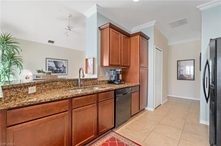 Kitchen with refrigerator, crown molding, sink, dark stone countertops, and black dishwasher
