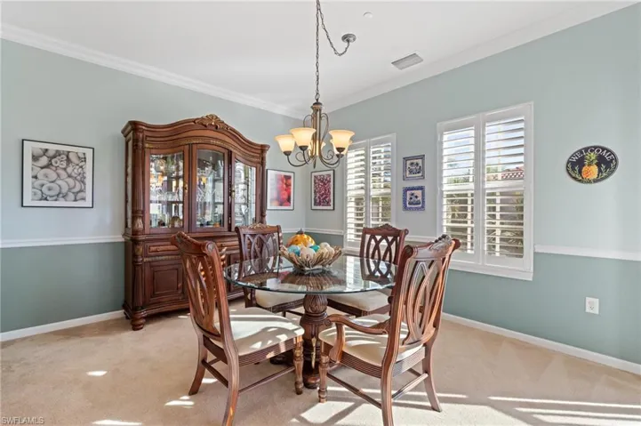 Carpeted dining area with an inviting chandelier and ornamental molding
