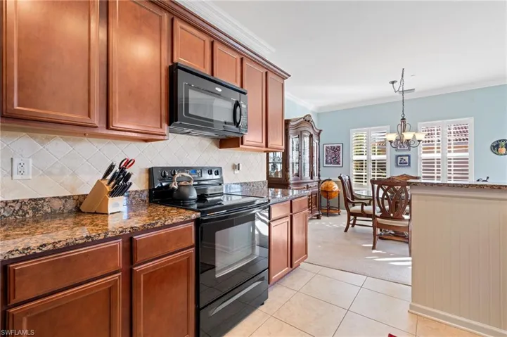 Kitchen with a notable chandelier, dark stone countertops, crown molding, light carpet, and black appliances