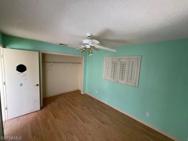 Unfurnished bedroom with a textured ceiling, wood finished floors, a ceiling fan, and a closet