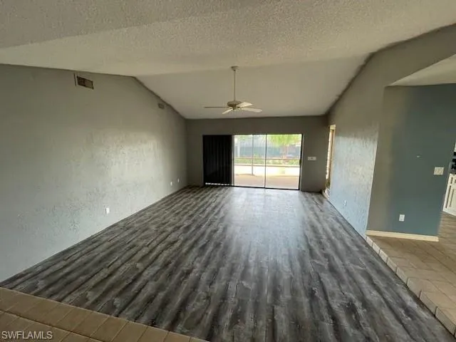 Unfurnished living room featuring a textured wall, a textured ceiling, wood finished floors, lofted ceiling, and ceiling fan