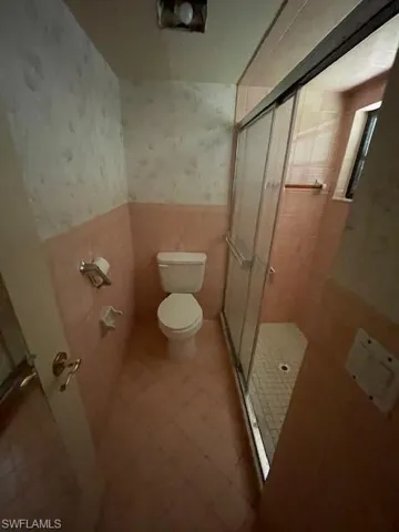 Bathroom with wallpapered walls, a stall shower, wainscoting, and tile walls