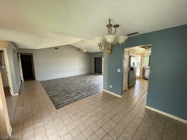 Tiled spare room with a ceiling fan, a textured ceiling, vaulted ceiling, and a chandelier
