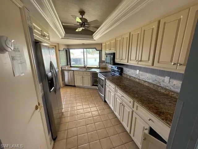 Kitchen featuring appliances with stainless steel finishes, a raised ceiling, ornamental molding, a ceiling fan, and dark stone counters