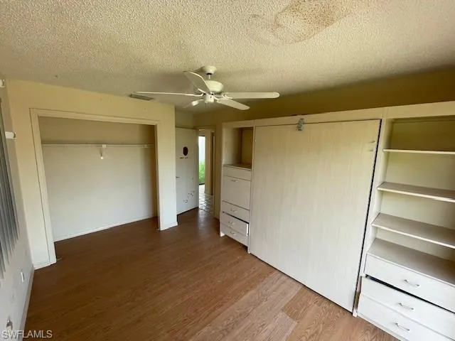 Unfurnished bedroom with dark wood-type flooring, a textured ceiling, ceiling fan, and a closet