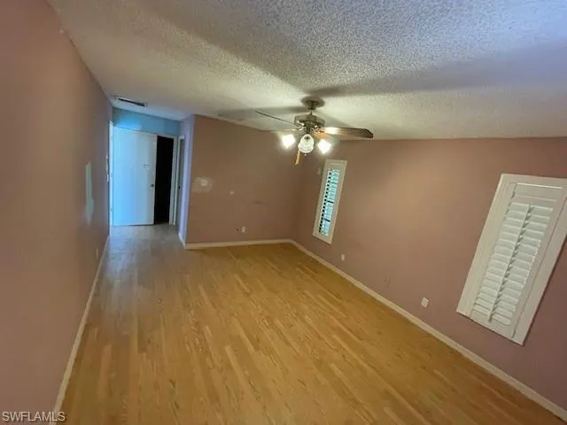 Empty room with a textured ceiling, light wood-type flooring, and ceiling fan