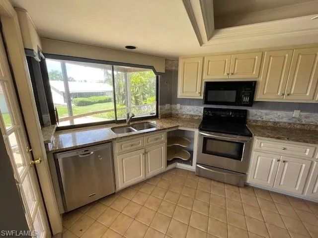 Kitchen with stainless steel appliances, dark stone countertops, light tile patterned floors, a tray ceiling, and crown molding